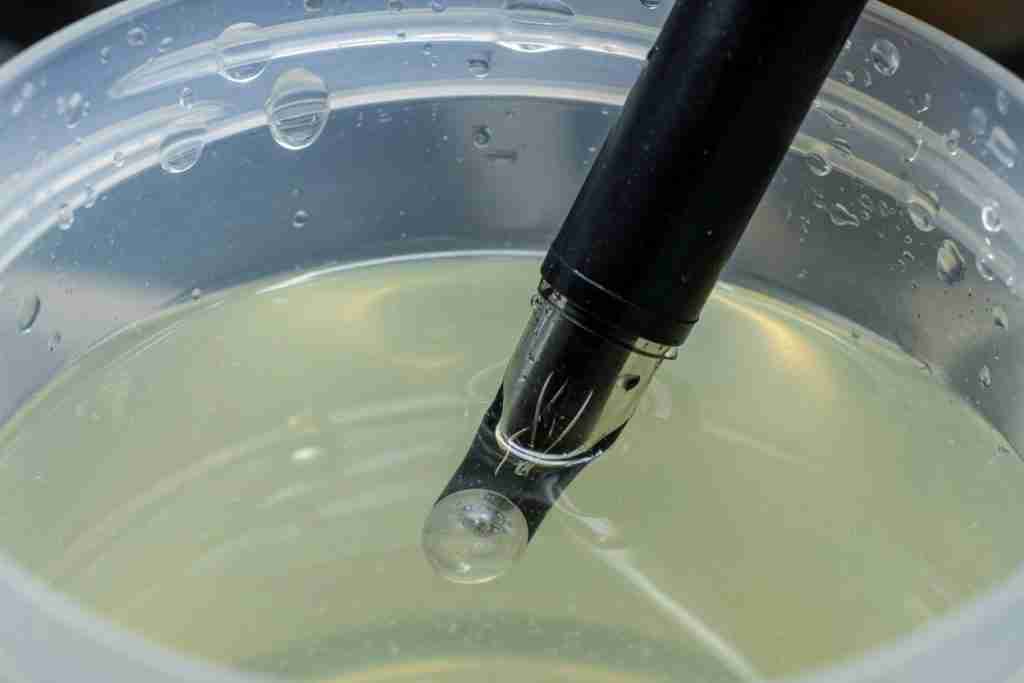 pH pen tip in a jug of pale foliar nutrient solution
