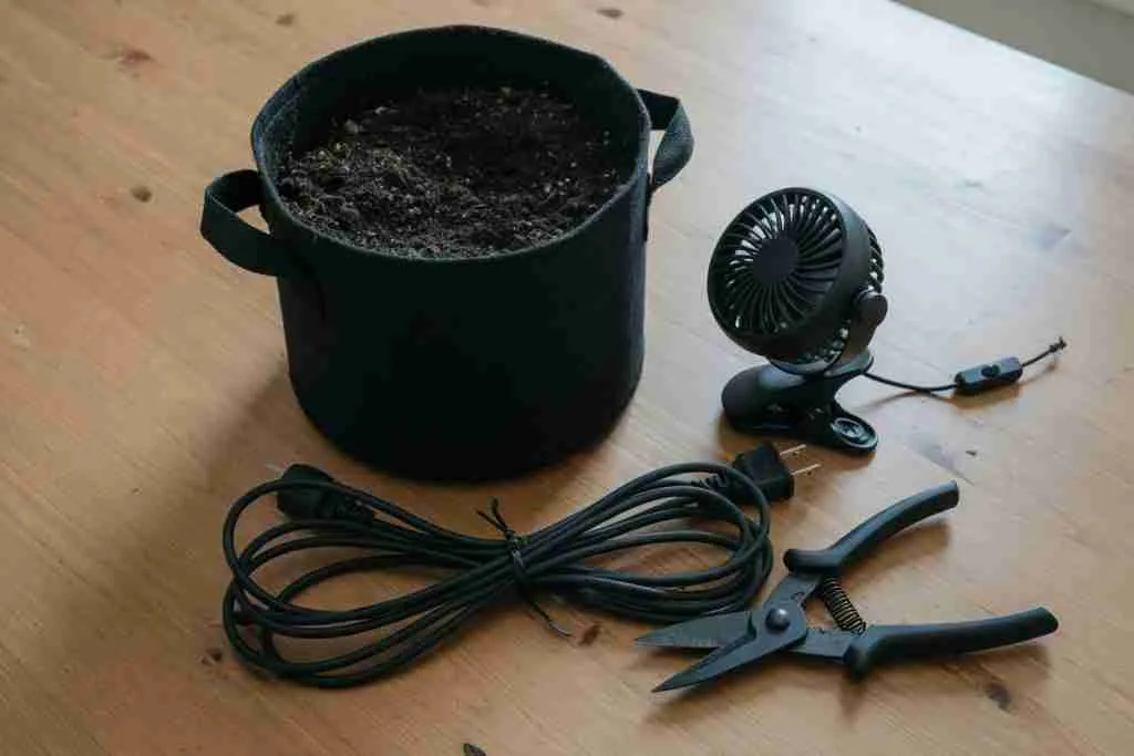 A fabric pot of soil, a small fan, a cord, and garden snips