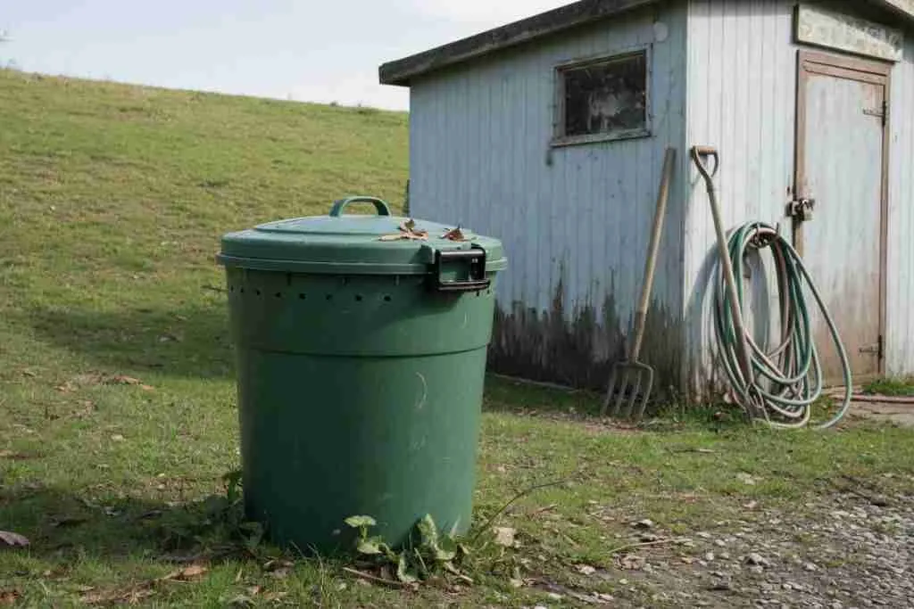 A small lidded compost bin beside a shed