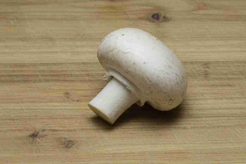 A single white button mushroom on a wood board